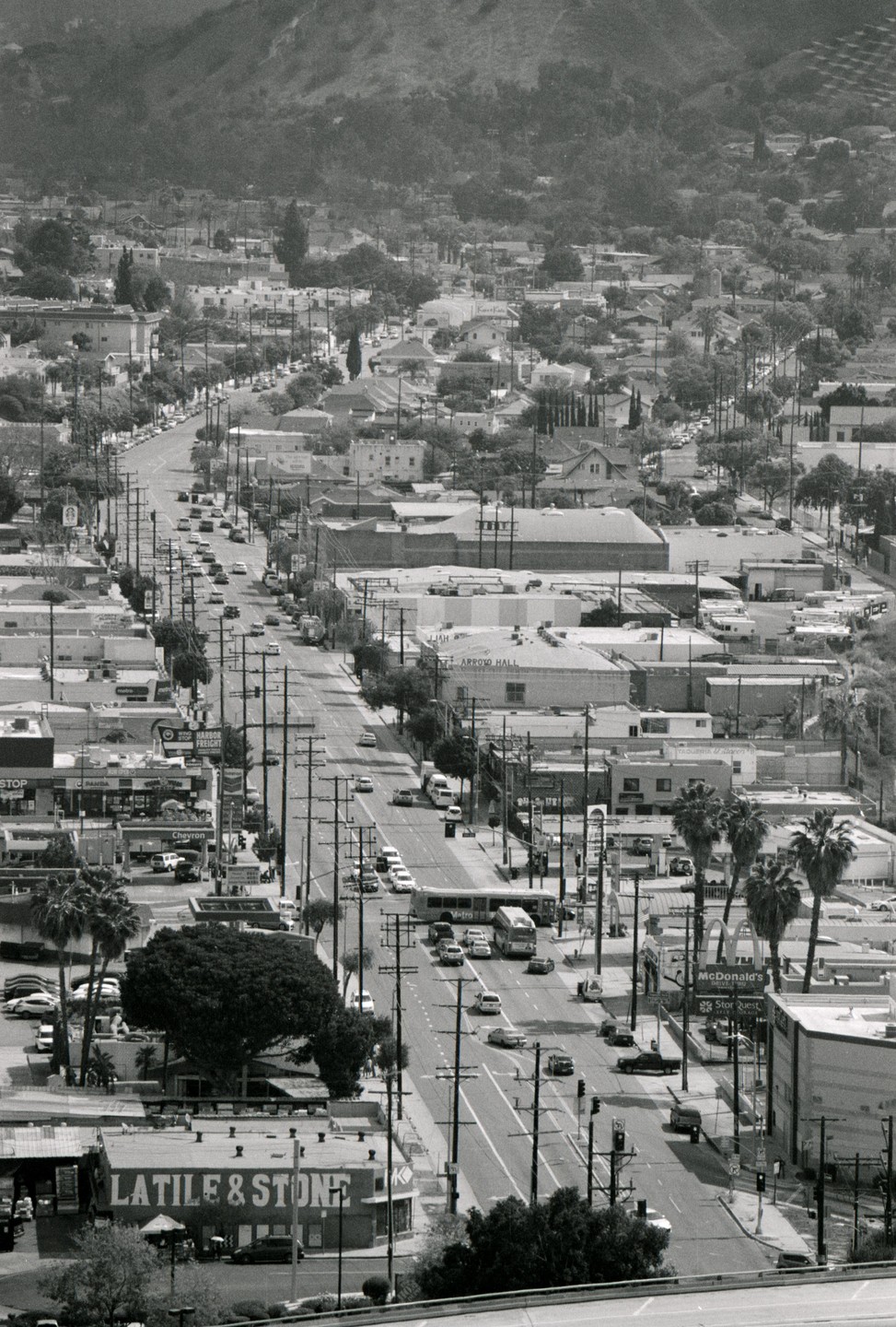A long street with cars and buildings is visible from an elevated perspective, with a mountain in the background.