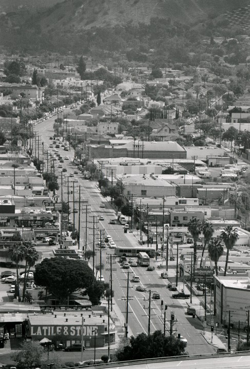 A long street with cars and buildings is visible from an elevated perspective, with a mountain in the background.