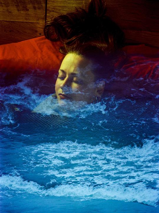 A woman with closed eyes is shown in a double exposure with ocean waves.