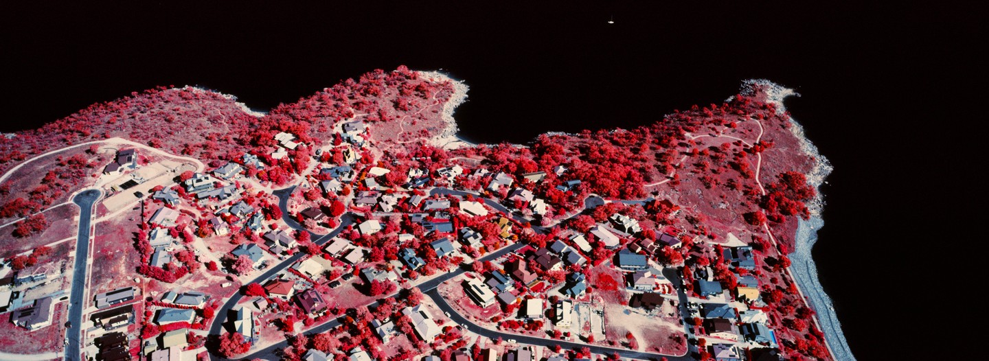 An aerial view shows a town with red trees and houses next to a body of water.