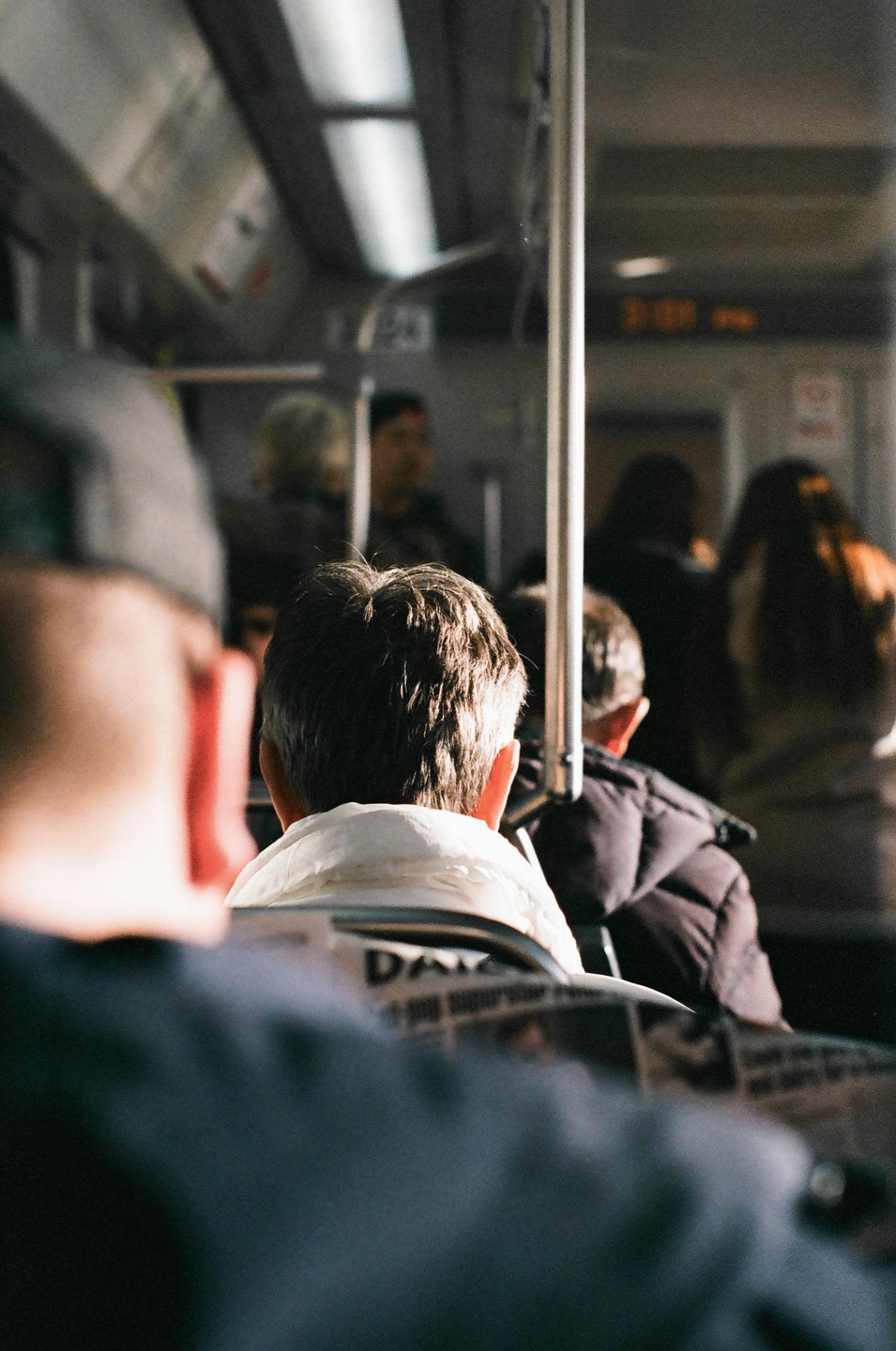 The back of a man's head is visible in the foreground, with other passengers in a train car behind him.