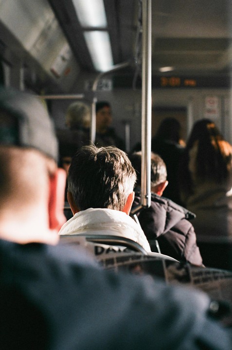 The back of a man's head is visible in the foreground, with other passengers in a train car behind him.