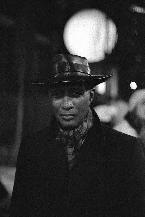 A man wearing a hat and scarf looks directly at the viewer.