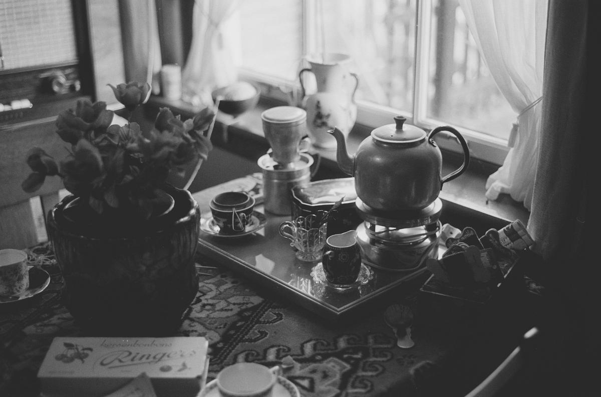 A teapot and cups are arranged on a tray next to a window with sheer curtains.