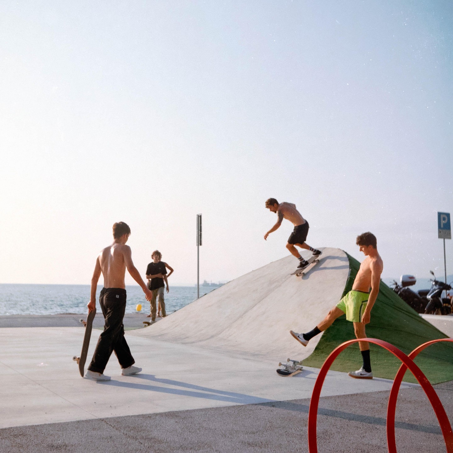 Four men are skateboarding on a concrete ramp next to the ocean.