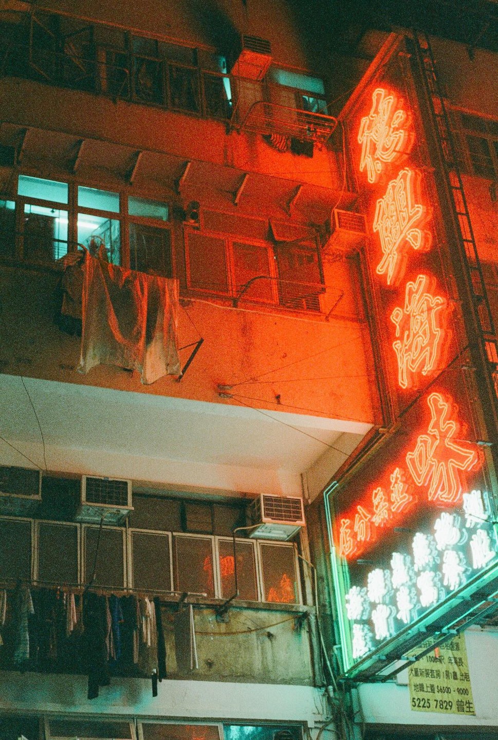 A building with clothes hanging to dry is illuminated by red and green neon signs at night.