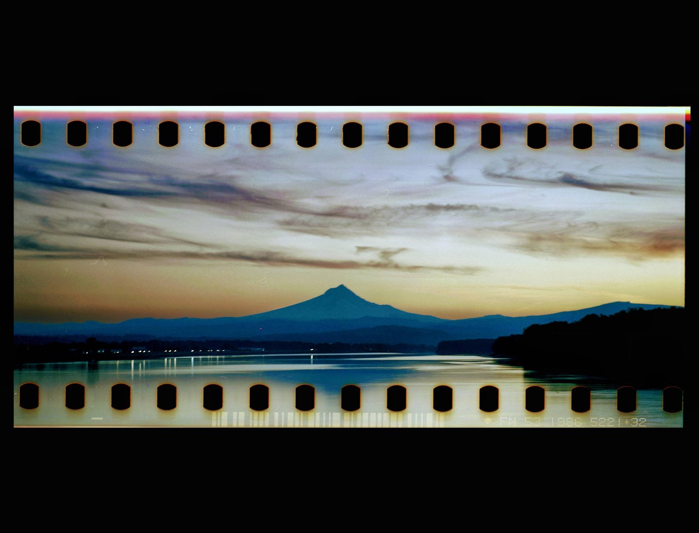 A mountain peak rises above a body of water with a cloudy sky at dusk.