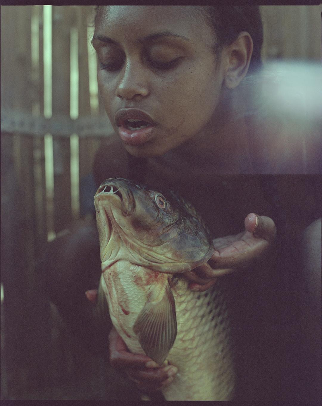 A girl holds a large fish with her eyes closed and mouth slightly open.
