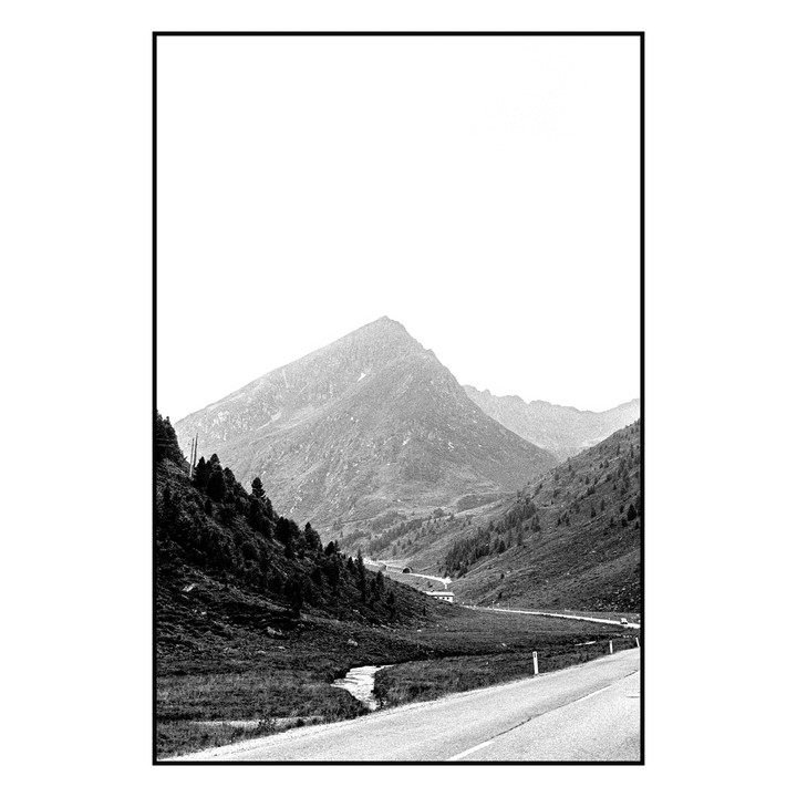 A winding road leads through a valley with mountains and trees under a bright sky.