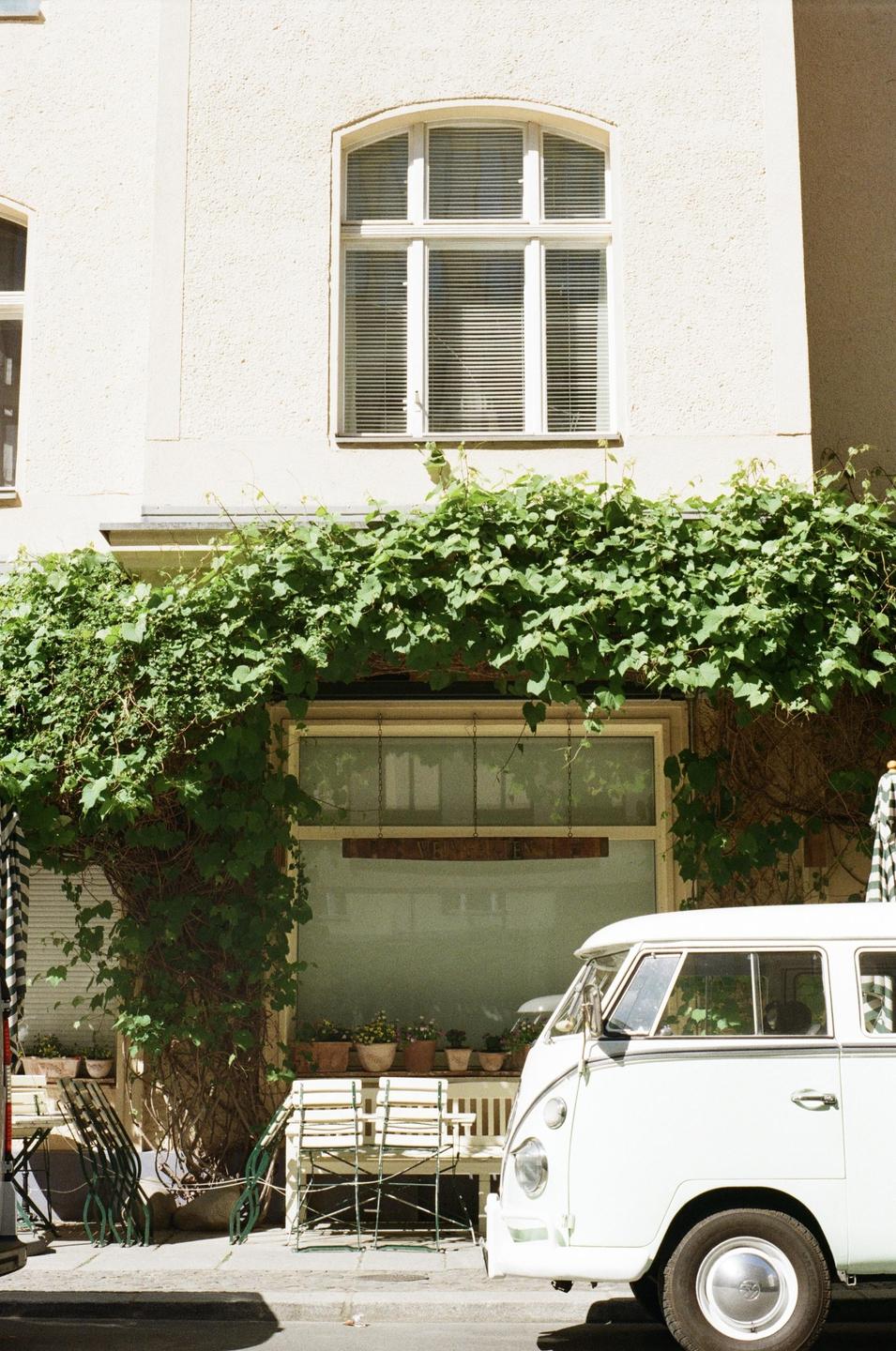 A white van is parked on a street in front of a building with green vines growing on it.