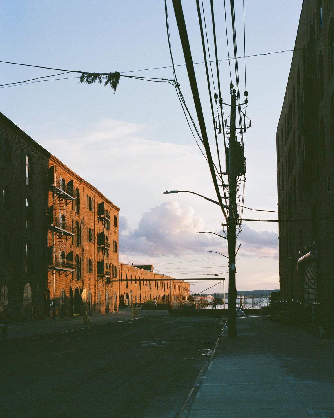 A street with brick buildings on either side leads to a body of water under a cloudy sky.