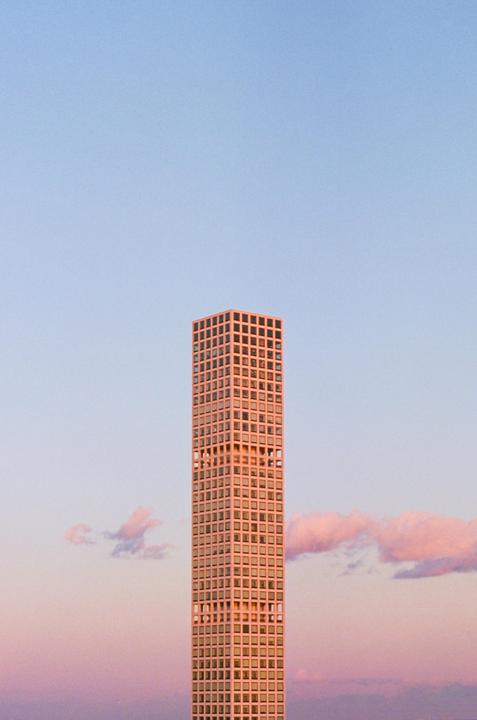 A tall, slender skyscraper with many windows stands against a sky with pink and blue hues.