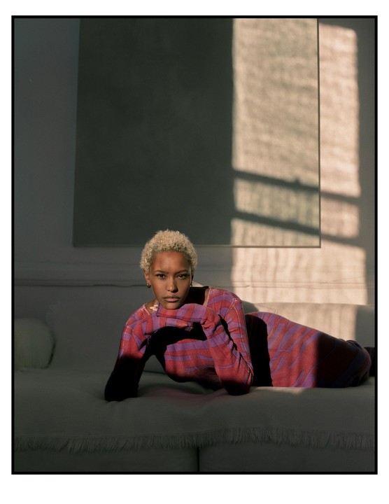 A woman with short, curly hair lies on a sofa, illuminated by a shaft of sunlight.
