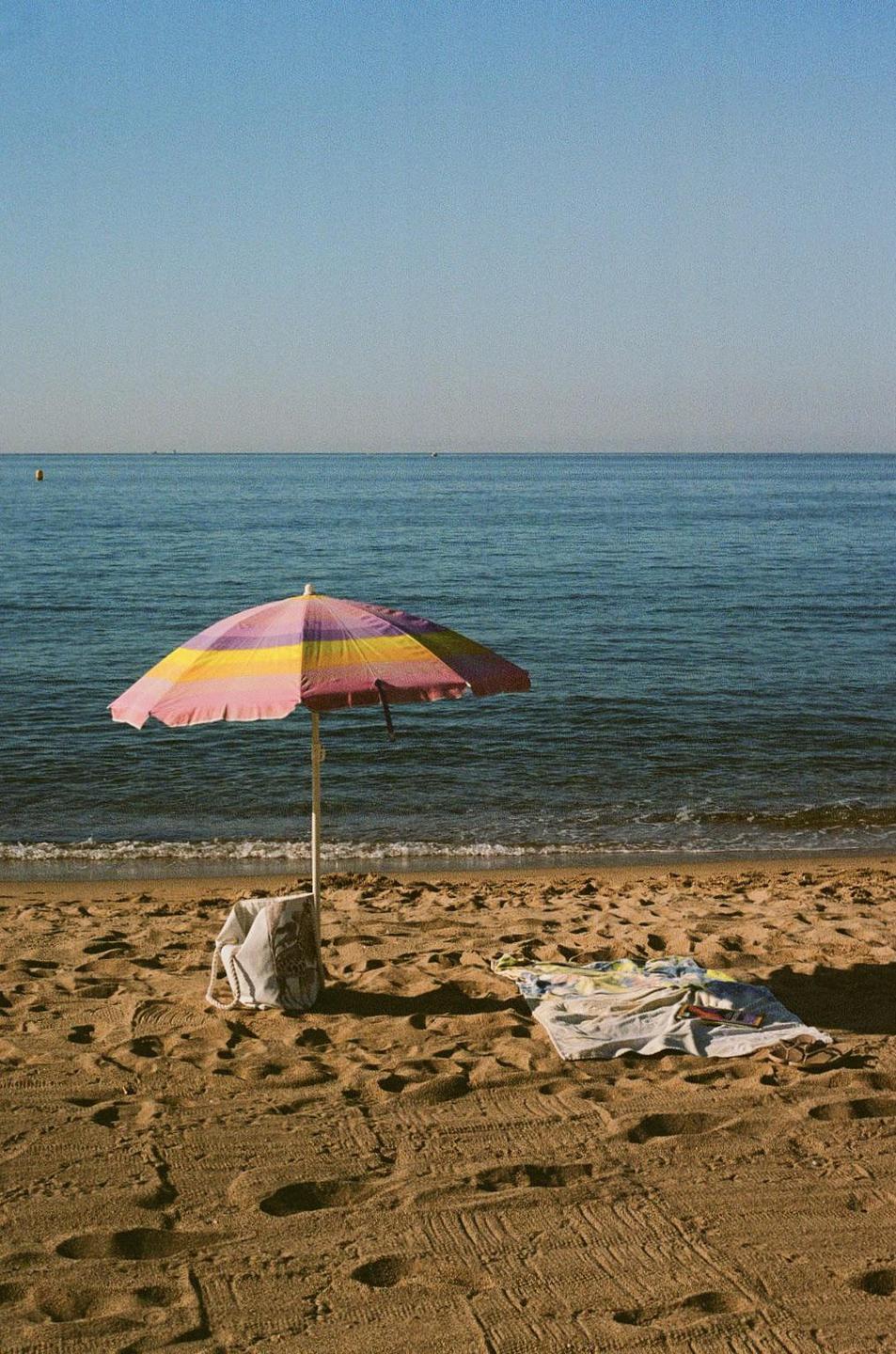 A colorful beach umbrella stands on a sandy beach next to the ocean.