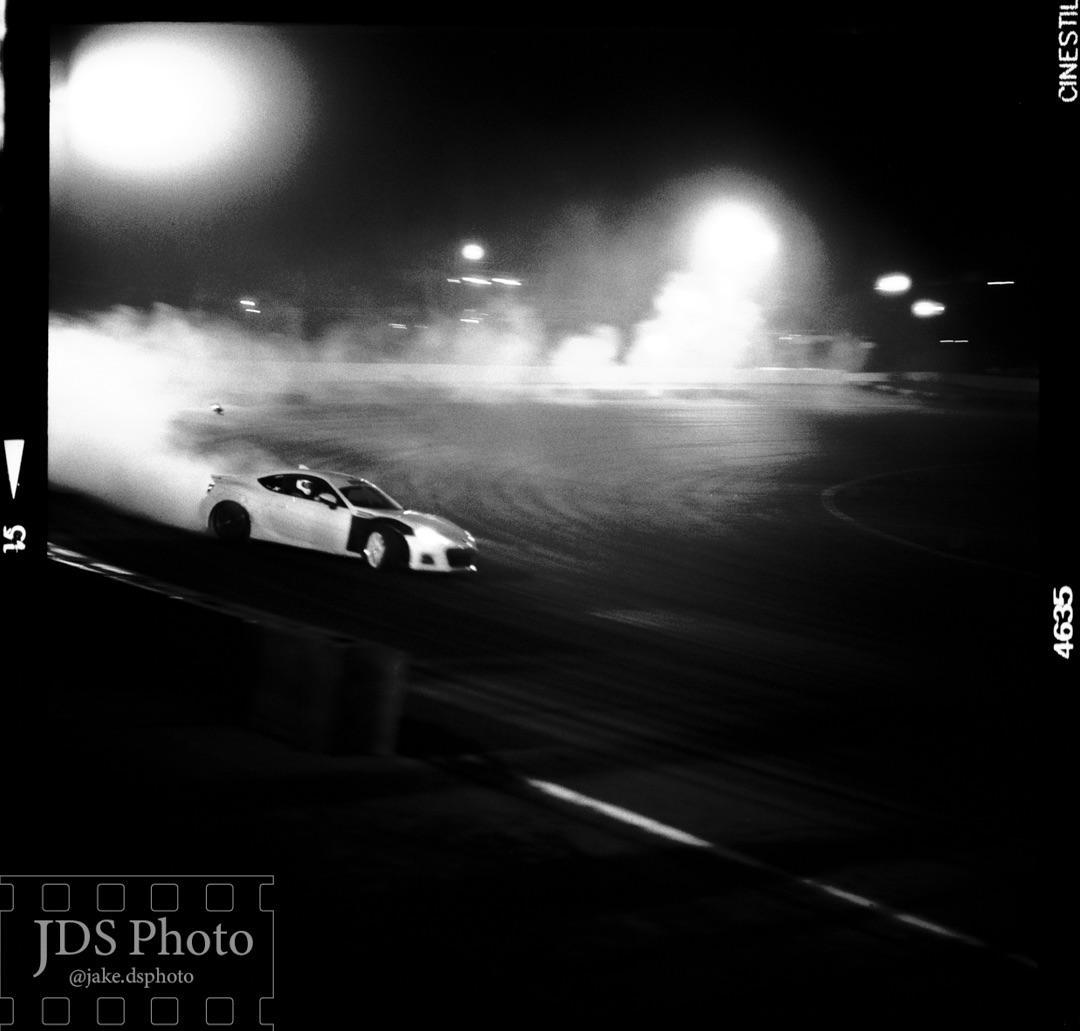 A white car drifts on a track at night, creating a large cloud of smoke.
