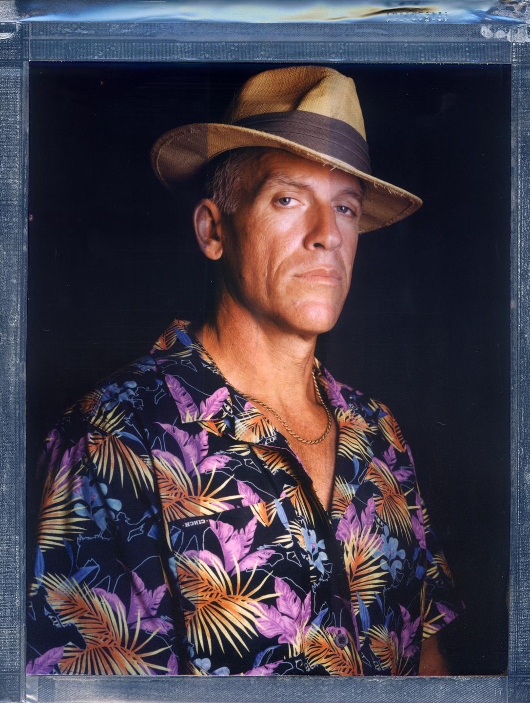 A man wearing a straw hat and a colorful shirt looks directly at the viewer.
