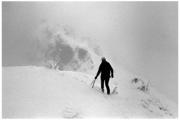 A person walks through a snowy landscape with an ice axe in hand.