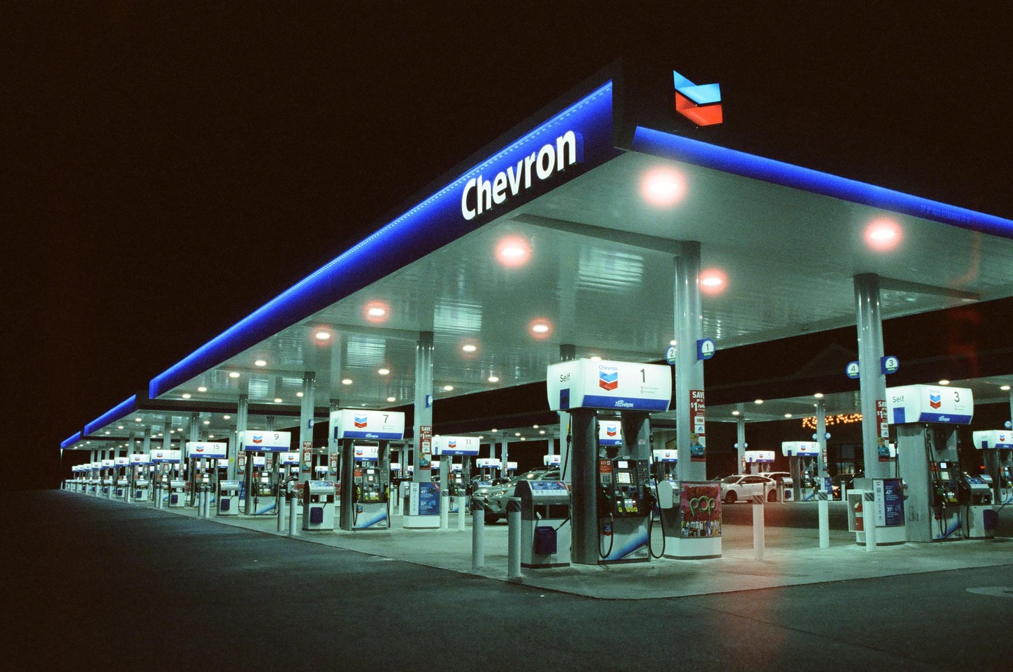 A Chevron gas station with many pumps is brightly lit at night.