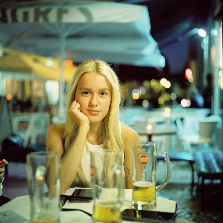 A woman with blonde hair rests her chin on her hand while sitting at a table with beer glasses at night.