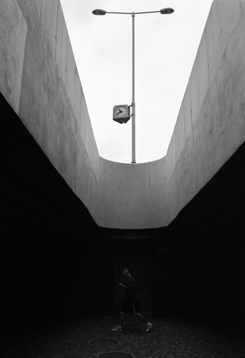 A man walks through a dark underpass with a clock and street light visible above.