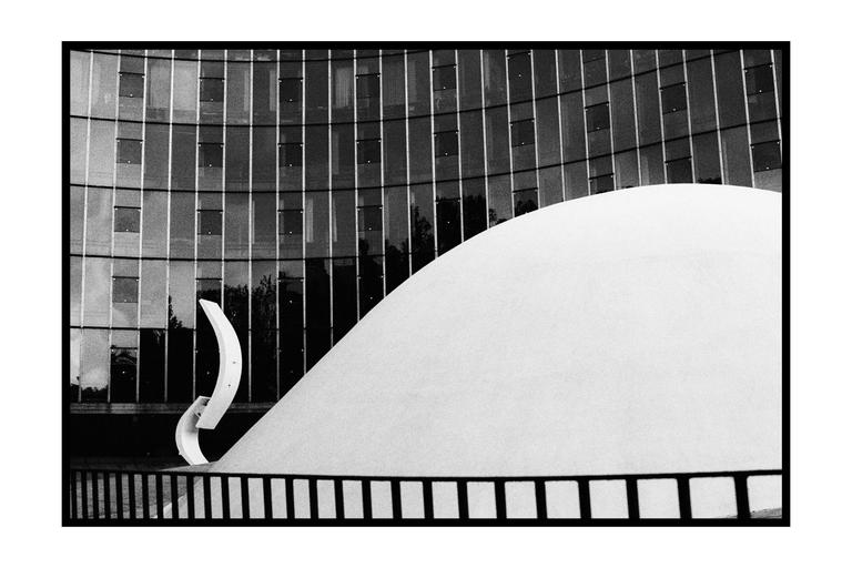 A large white dome is in front of a glass building with a black fence in the foreground.