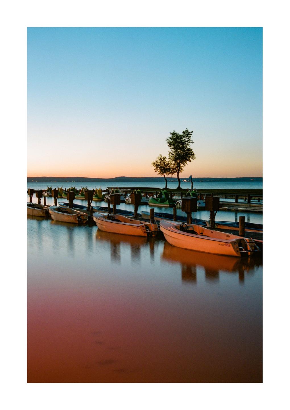 Small boats are docked on a lake at dusk, with a warm glow on the water.