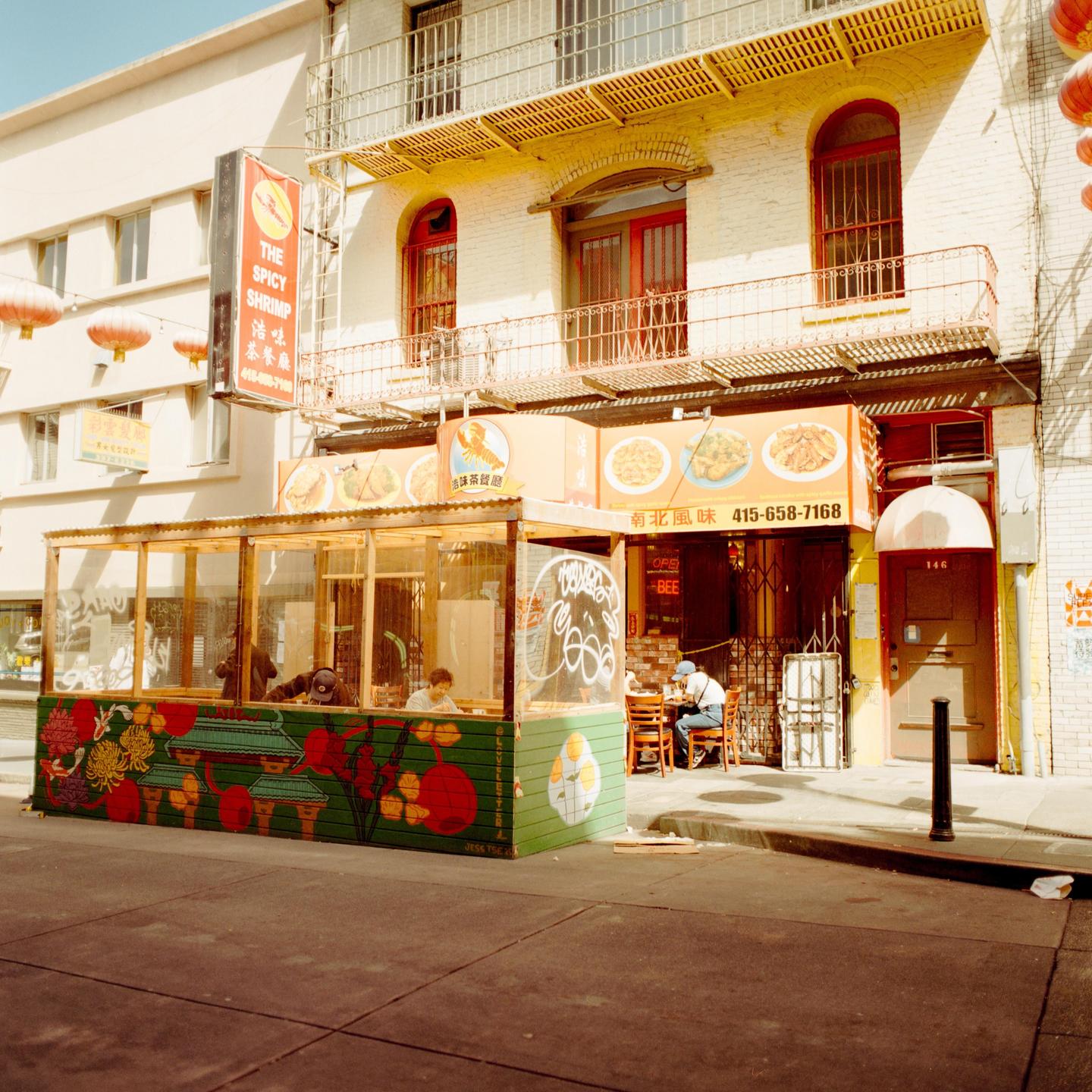 A street view shows a restaurant with an outdoor dining area and people seated inside and outside.