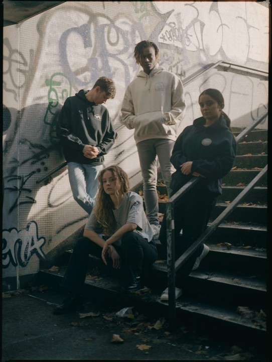 Four young people pose on a concrete staircase with graffiti-covered walls.