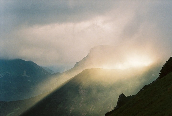 Sunlight breaks through clouds, illuminating a mountain range.