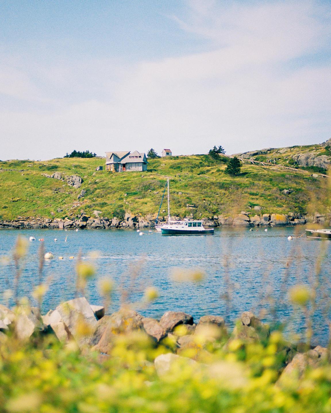 A sailboat is moored in a bay with a house on a grassy hill in the background.