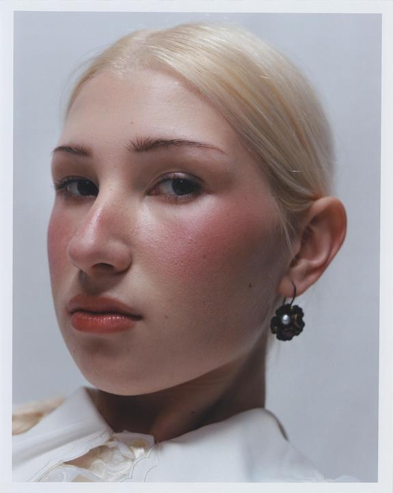 A woman with blonde hair and rosy cheeks looks directly at the viewer.