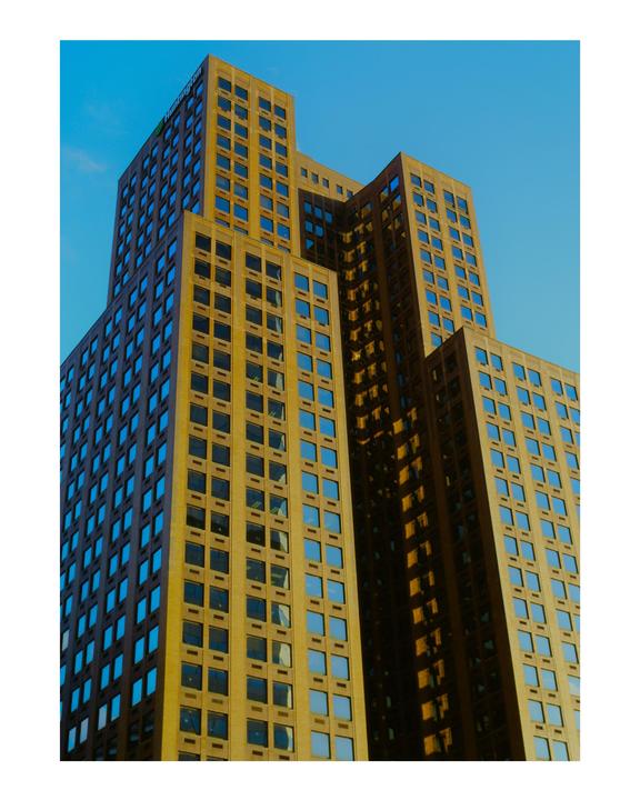 A tall building with many windows is photographed from a low angle against a clear blue sky.