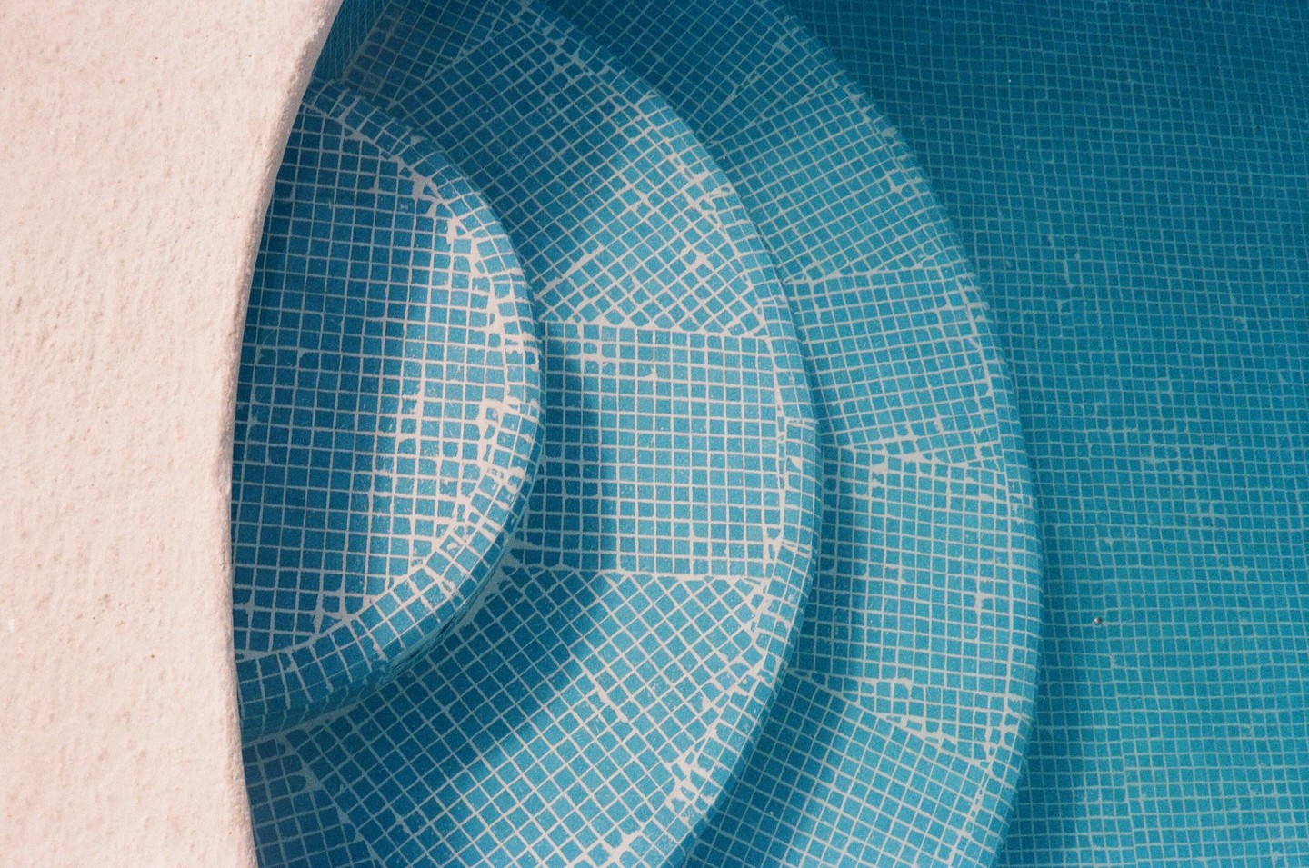 The steps of a swimming pool are visible, covered in blue and white tiles, with a white edge on the left.