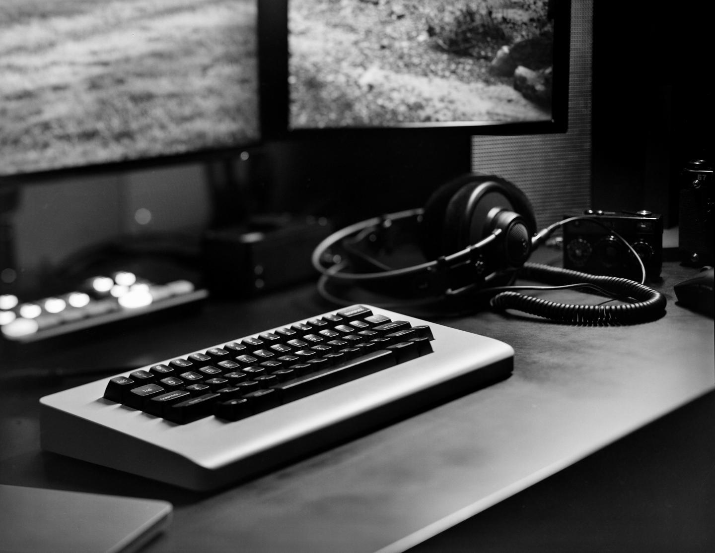 A keyboard, headphones, and camera are arranged on a desk in front of two computer monitors.