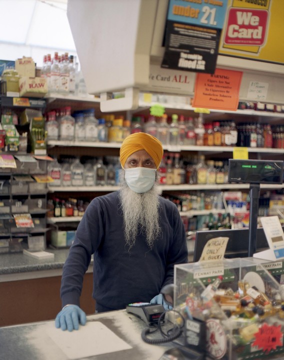 A man wearing a yellow turban, a white face mask, and blue gloves stands behind a counter in a store.