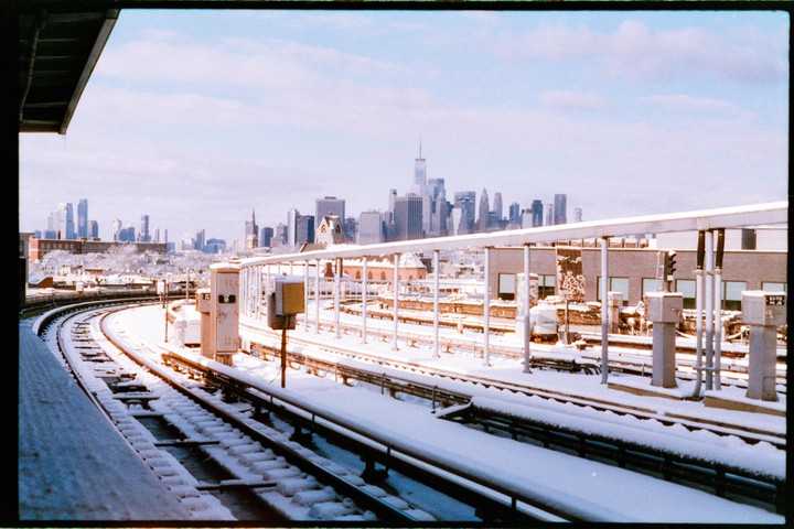 Snow-covered train tracks curve towards a distant city skyline under a bright sky.
