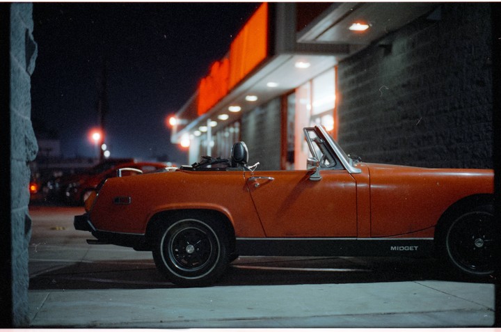 An orange convertible car is parked at night in front of a building with bright orange and white lights.