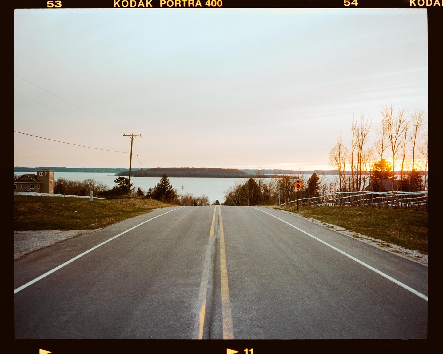 A road leads down to a body of water with a sunset on the horizon.
