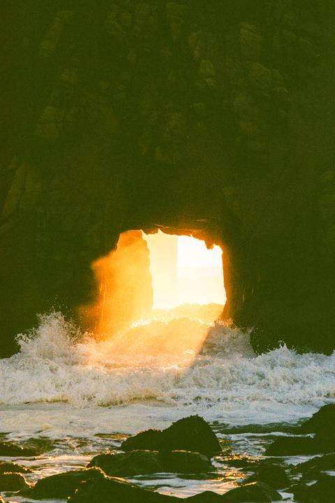 Waves crash through a dark sea cave illuminated by bright golden light.