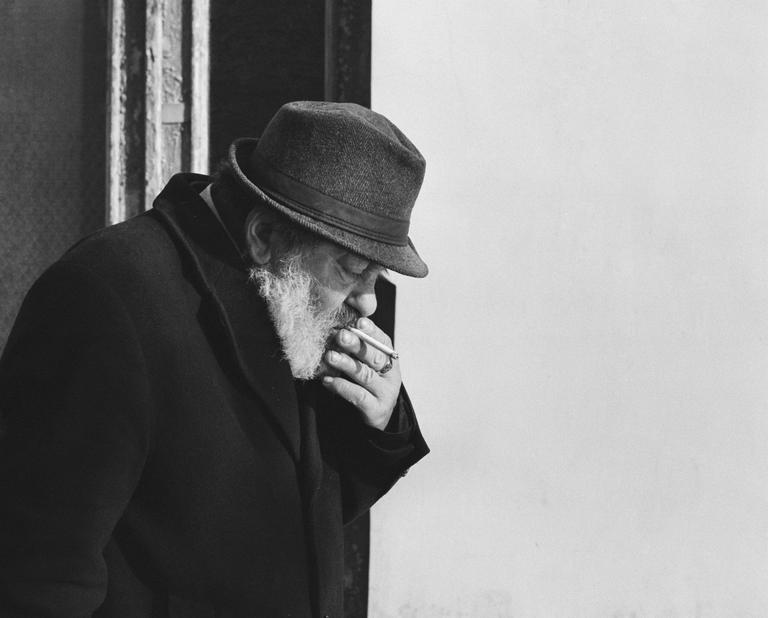 A man with a beard and hat is smoking a cigarette.