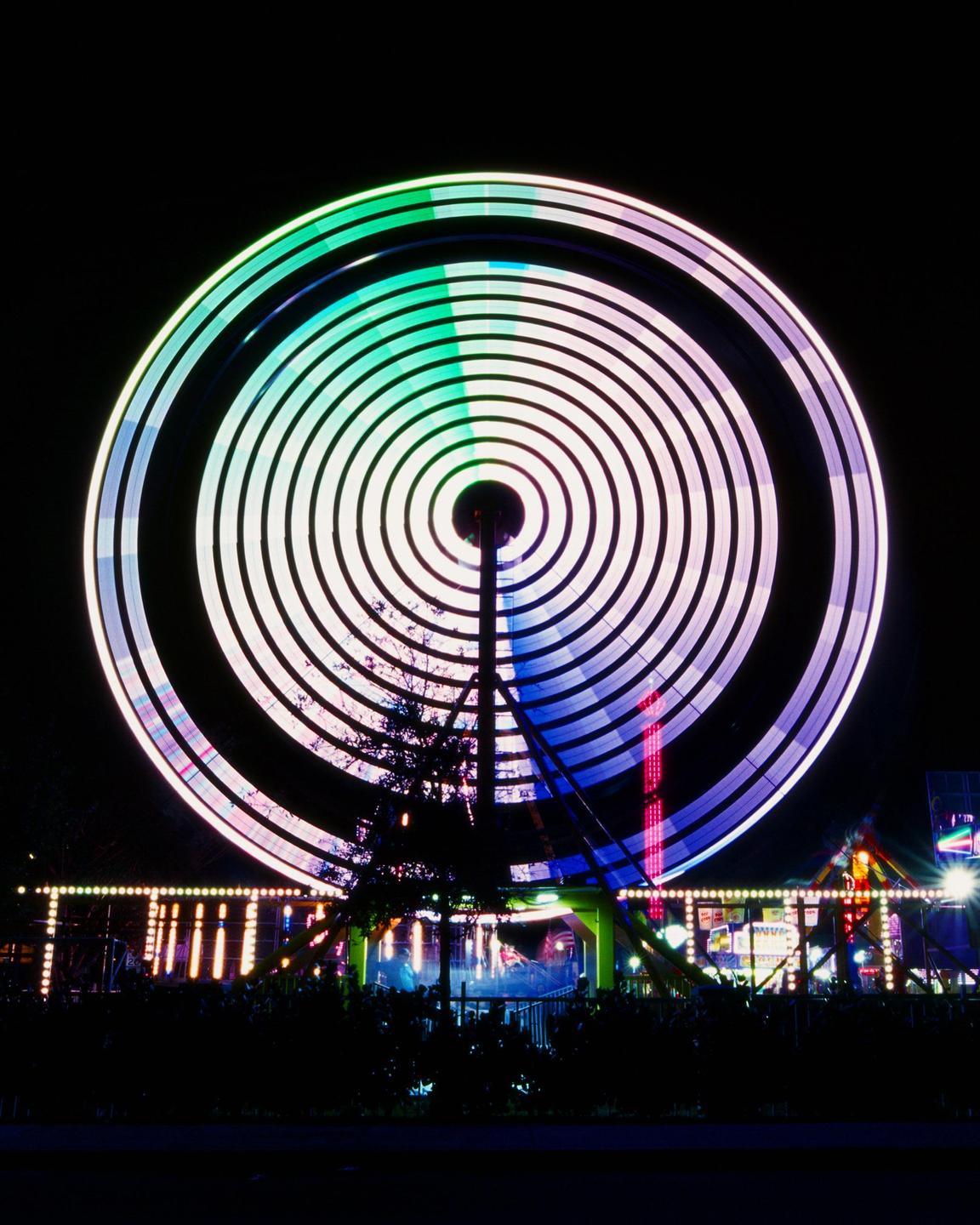 A long exposure shot of a ferris wheel at night creates a circular light trail.