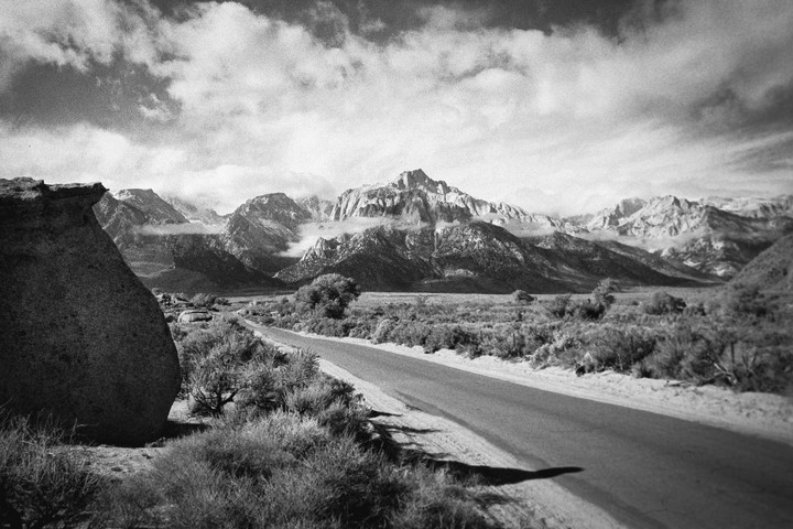 A road leads toward a mountain range with clouds partially obscuring the peaks.