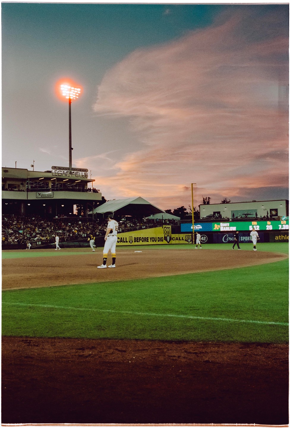 A baseball player stands on the field during a game at sunset.