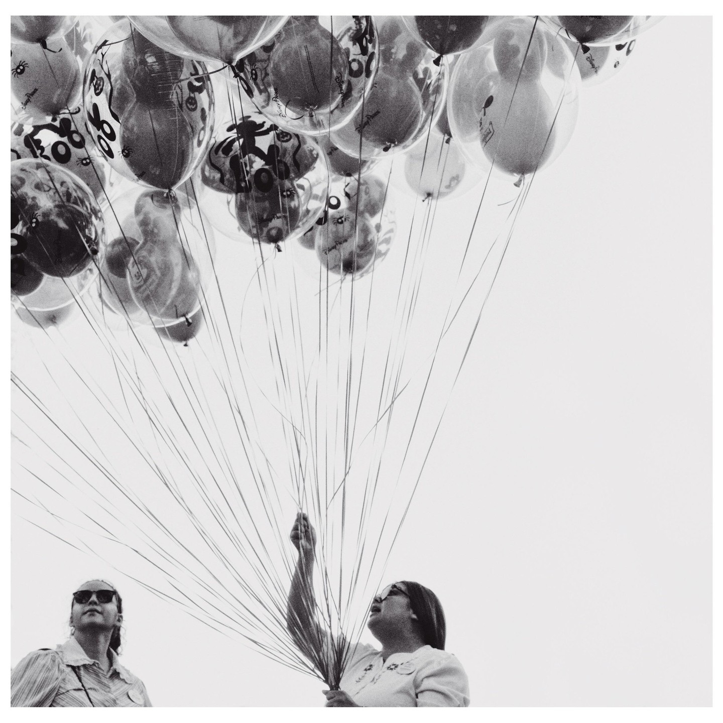 Two women look up at a large bunch of balloons with cartoon characters on them, held by one of the women.