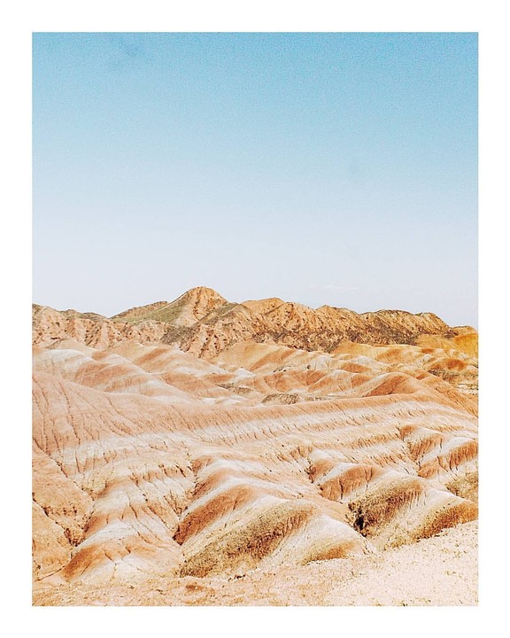 A vast desert landscape features rolling hills and mountains under a clear sky.
