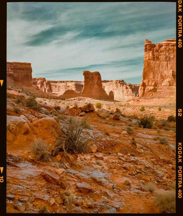 A desert landscape features red rock formations under a blue sky with wispy clouds.
