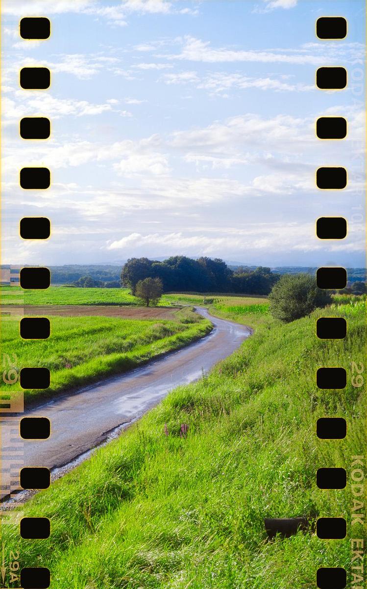 A winding road cuts through green fields under a cloudy sky.