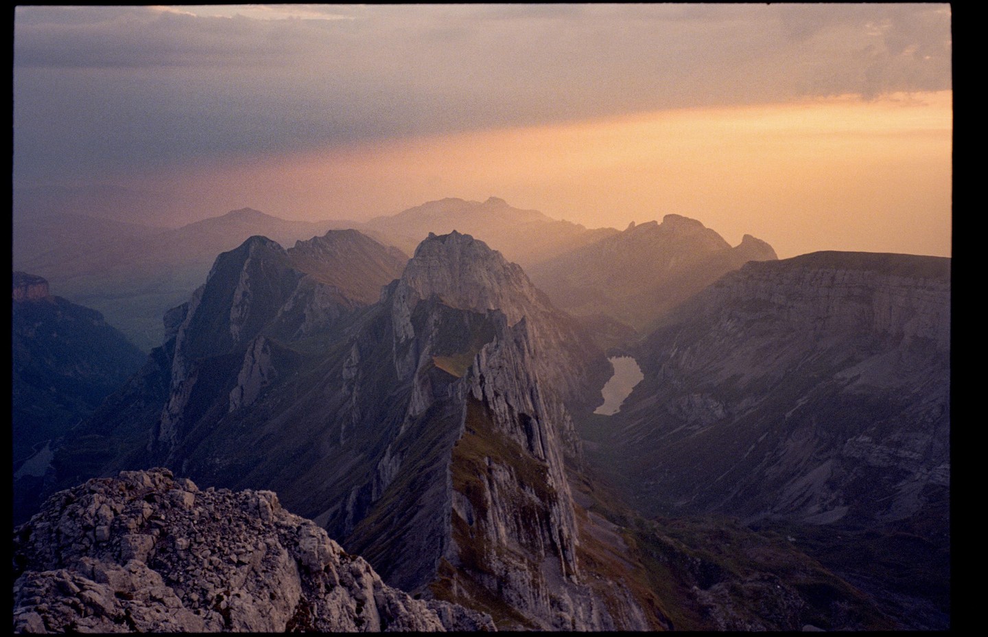 A mountain range with a lake in the distance is illuminated by a ray of sunlight breaking through the clouds.
