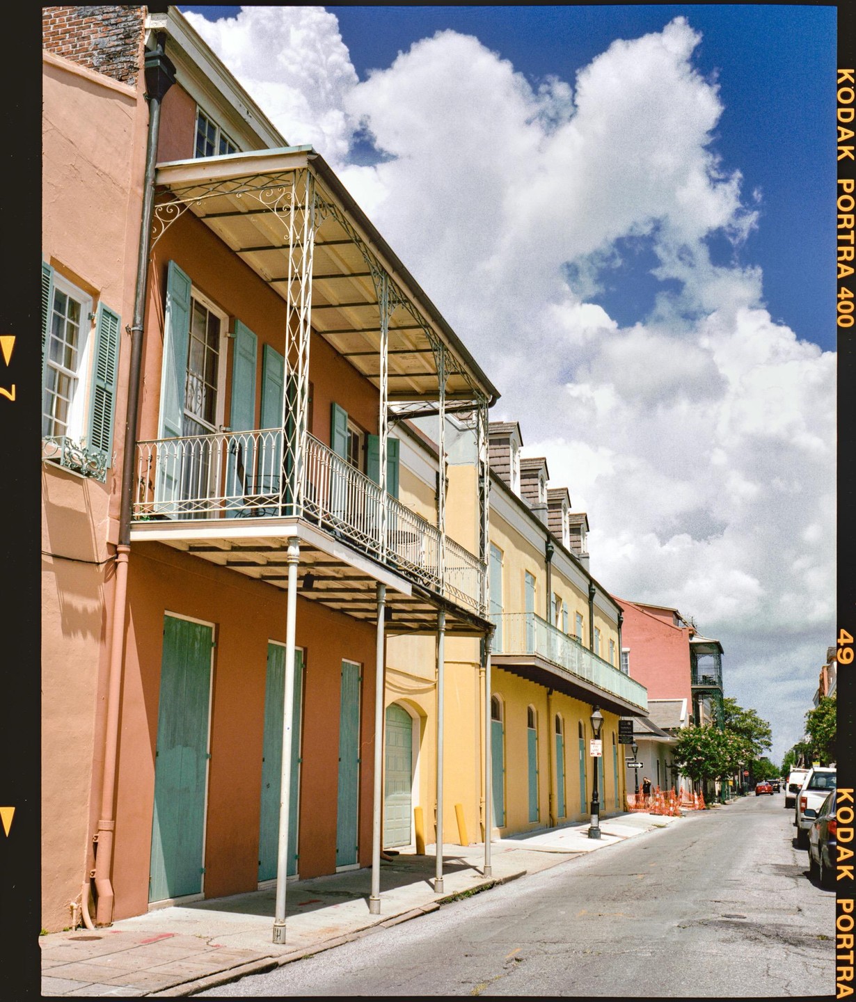 A street in the French Quarter is lined with colorful buildings featuring balconies and shutters under a bright blue sky with white clouds.