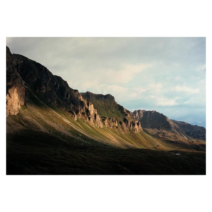 A dramatic landscape shows a mountain range with a valley in shadow and sunlit peaks under a cloudy sky.